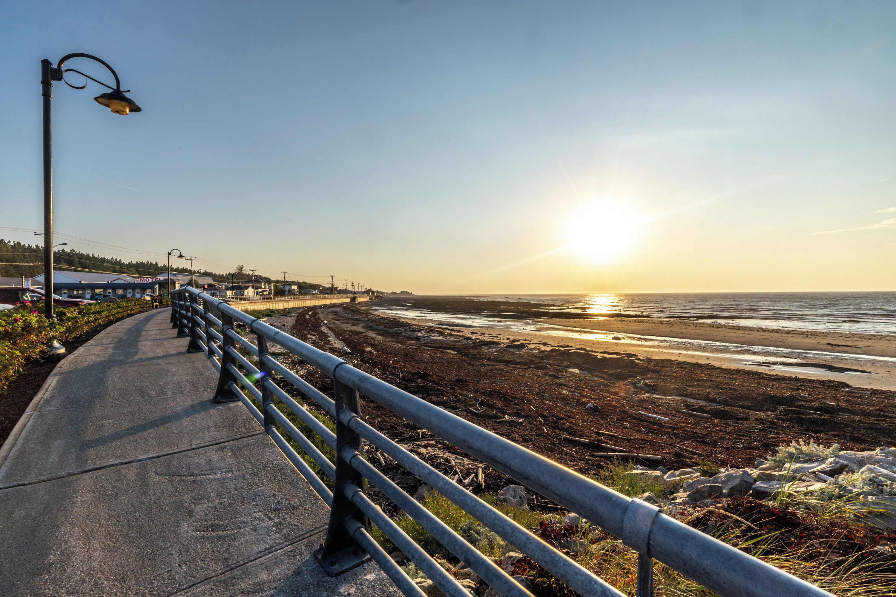 A coastal walkway with a metal railing, a street lamp, and a view of the ocean during sunset.