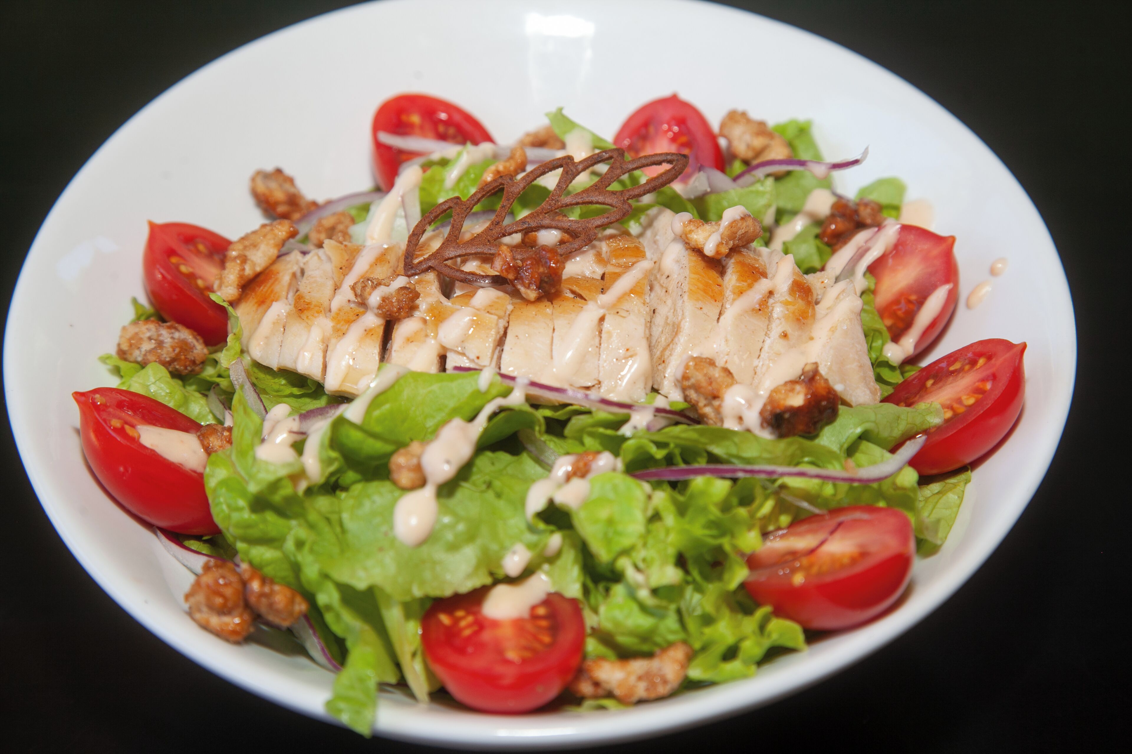 A salad with lettuce, tomatoes, and chicken on a white plate.