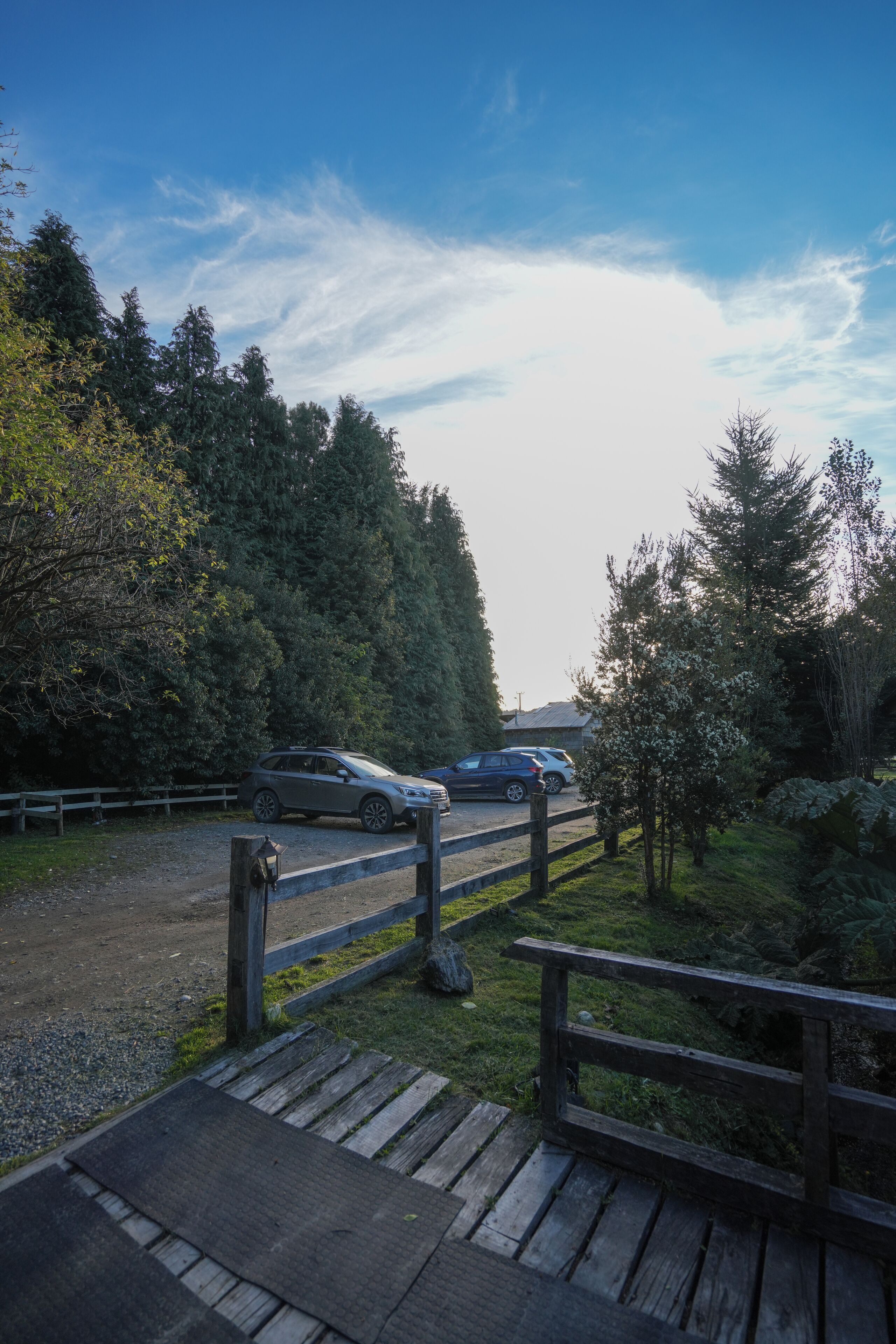 A wooden deck leading to a parking area with two cars parked.