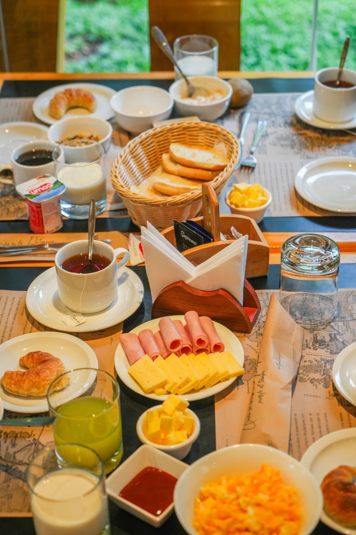 Una mesa de desayuno con cruasanes, queso, jamón y diversas bebidas.