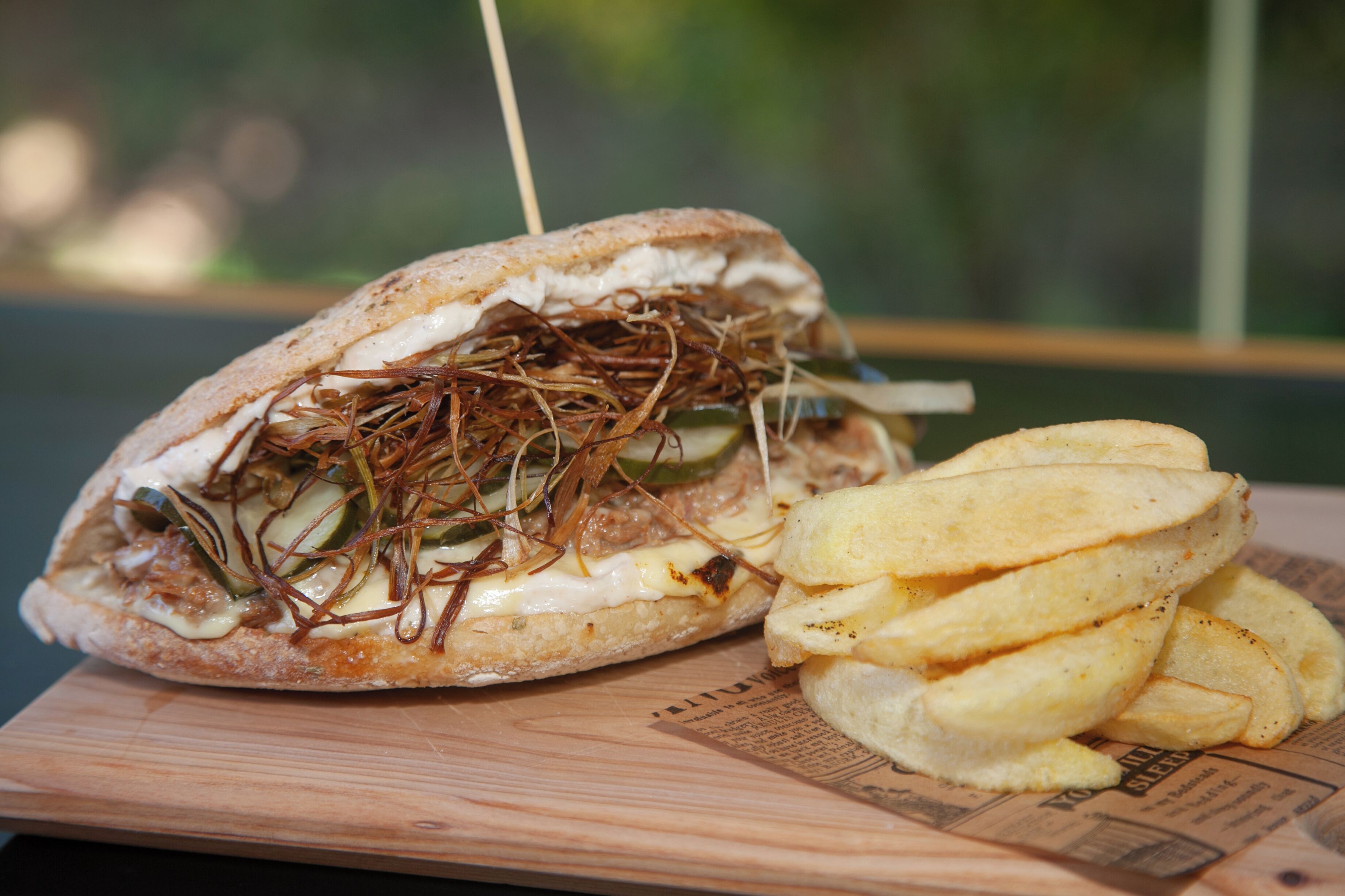 Un sándwich con pepinillos y una porción de papas fritas sobre una tabla de madera.