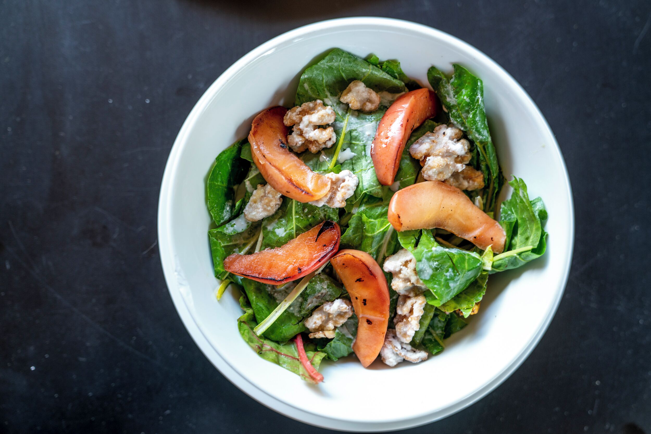 Un tazón de ensalada con hojas verdes, tomates y nueces.