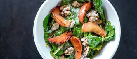 Un tazón de ensalada con hojas verdes, tomates y nueces.
