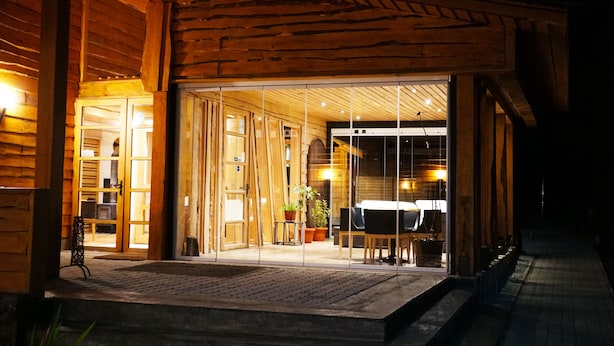 Un bâtiment en bois avec une entrée en verre, un chemin en briques et des plantes en pot à l’intérieur.