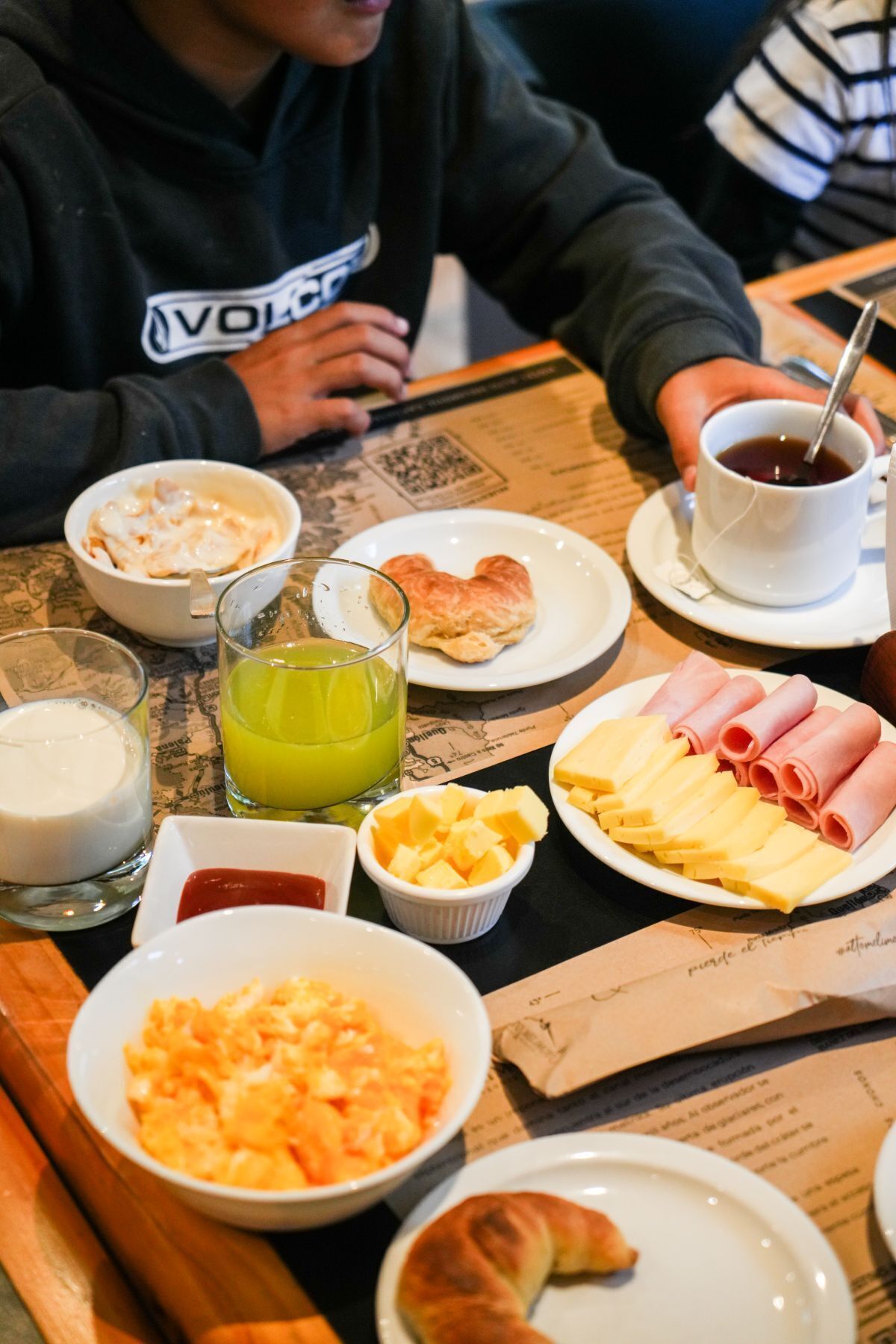 Ruokapöytä, jonka päällä on erilaisia aamiaisherkkuja, kuten munia, kinkkua, juustoa ja croissant.