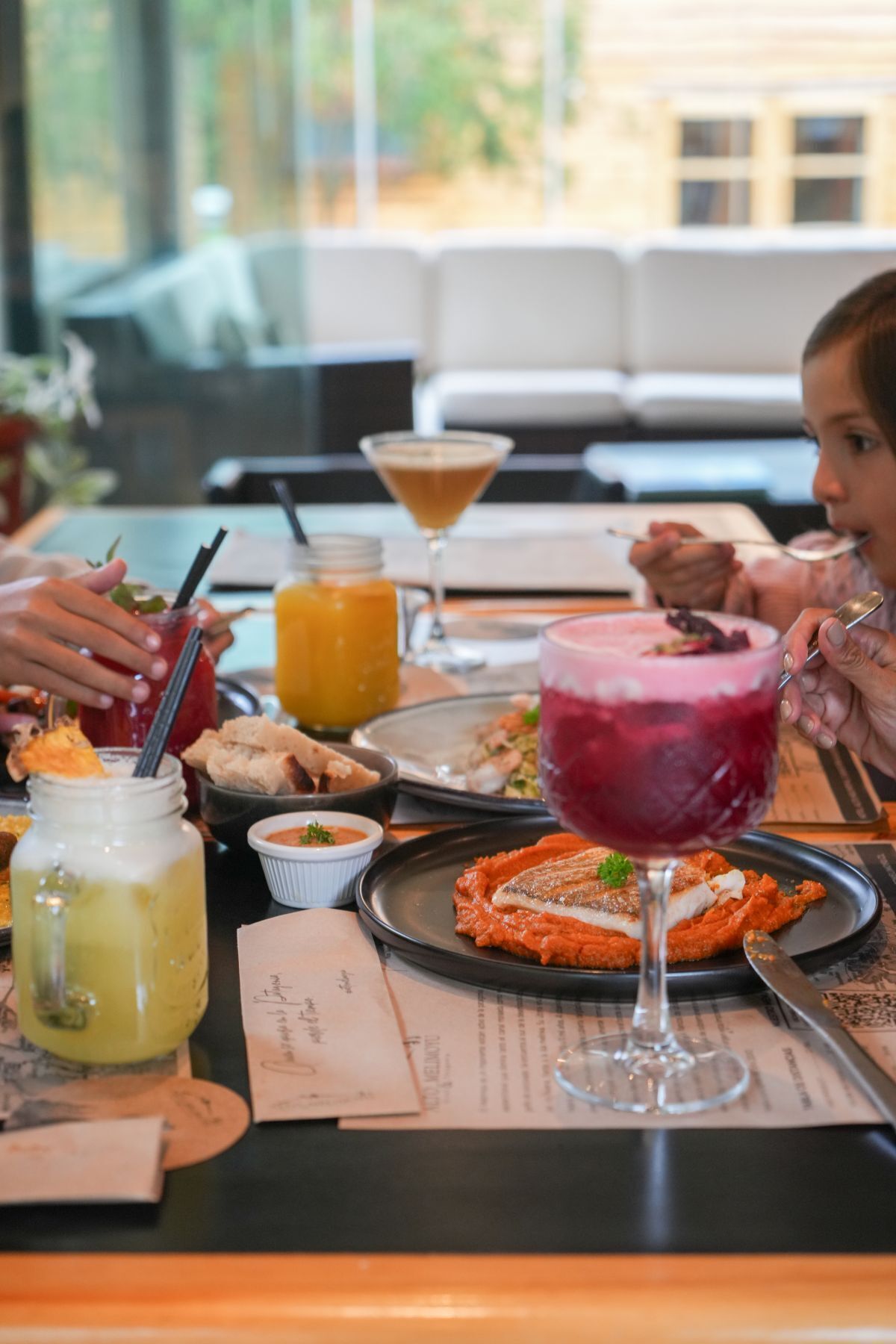 A restaurant setting with a table set for a meal, including a variety of drinks and a dessert.