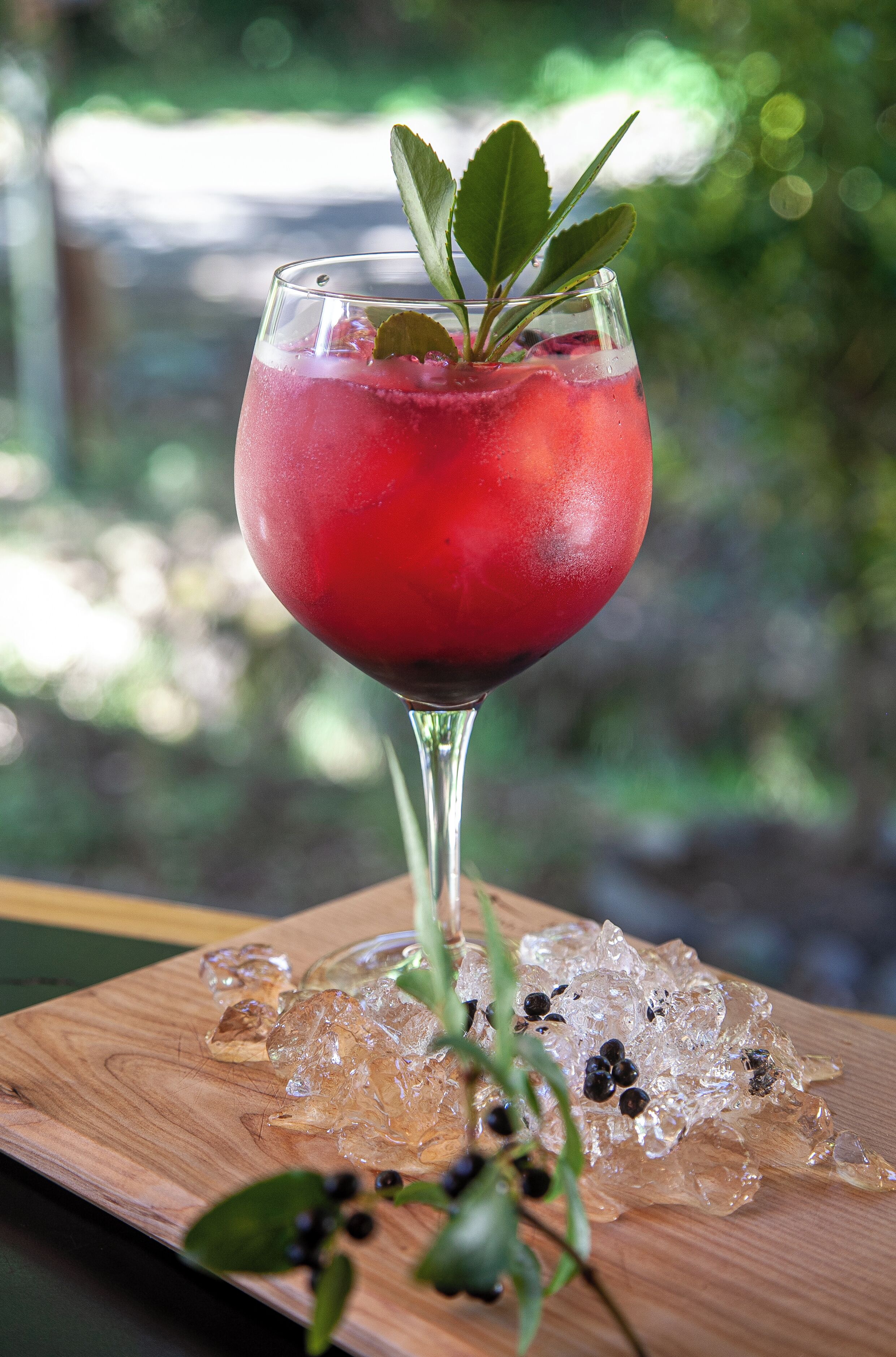 Un vaso de bebida roja con adorno de menta sobre superficie de madera, con hielo y bayas.