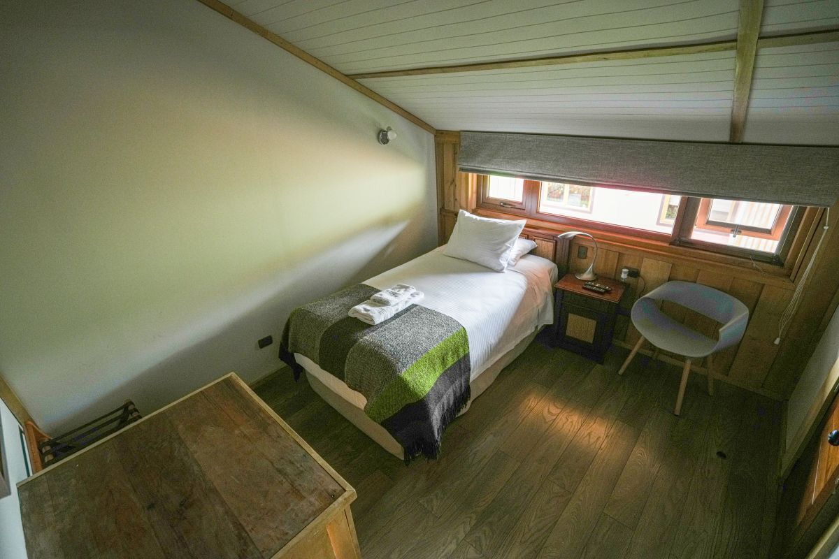 Ein kleines, gemütliches Schlafzimmer mit einem Bett, einem Nachttisch, einem Stuhl und einem Fenster.