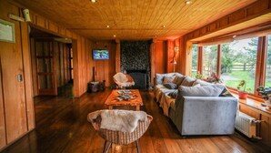 A cozy wooden interior with a fireplace, comfortable seating, and large windows. - Hotel Alto Melimoyu (Cisnes)