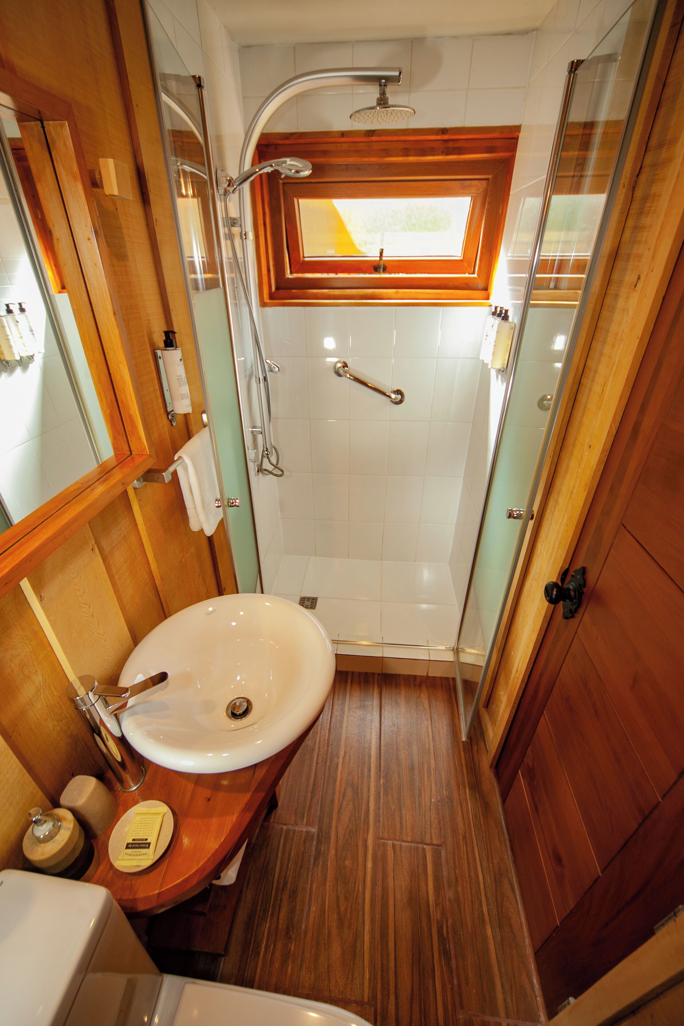 A compact bathroom with a wooden vanity, a sink, and a shower enclosure.