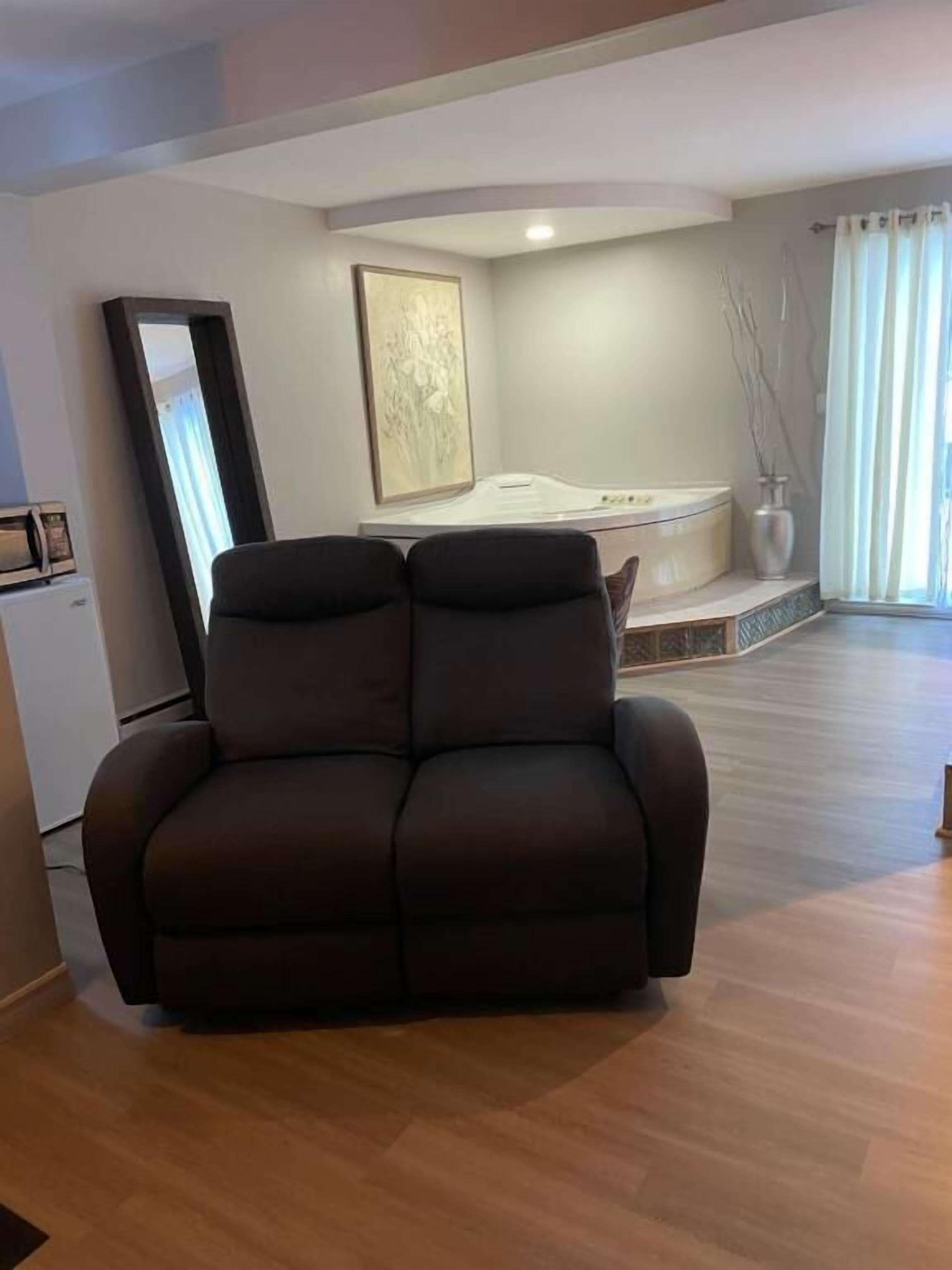 A living room with a dark-colored sofa, a large painting on the wall, and a bathtub in the background.