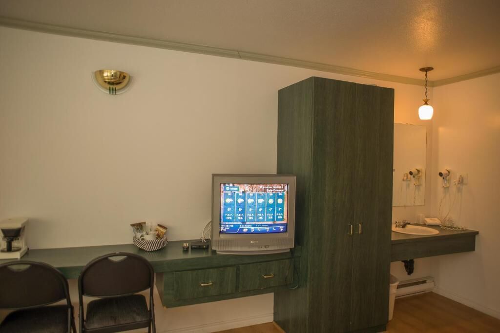 Une pièce avec un téléviseur posé sur un meuble en bois, un évier et un miroir au-dessus.