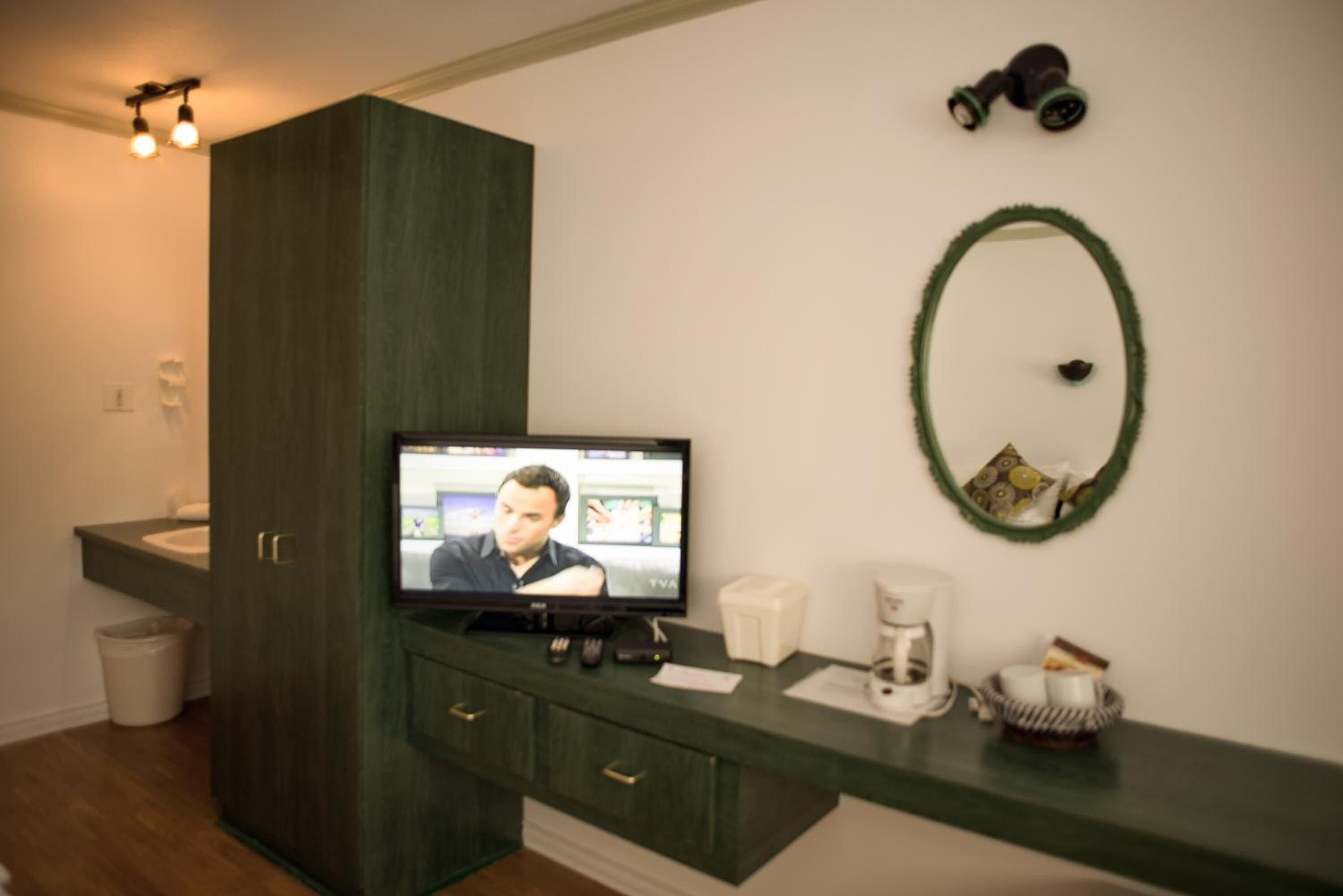 Ein Badezimmer mit einem dunklen Holzschrank, einem Spiegel, einem Fernseher und einer Kaffeemaschine.