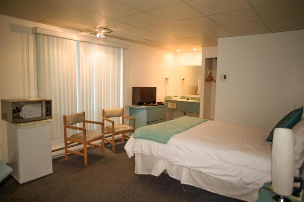 Une chambre d’hôtel équipée d’un lit, d’un bureau, d’une chaise, d’une télévision, d’un miroir et d’une fenêtre avec des stores.