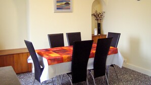 A dining area with a table set for six, chairs, a clock, and a framed picture on the wall. - Haven Cottage (Seahouses)