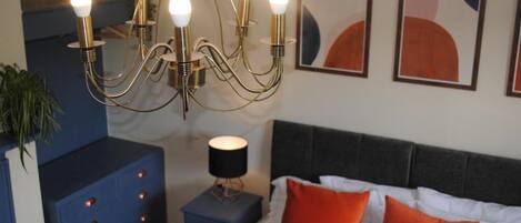 Une chambre à coucher comprenant un lit, une table de chevet, une commode, un lustre et des œuvres d’art abstraites accrochées au mur.
