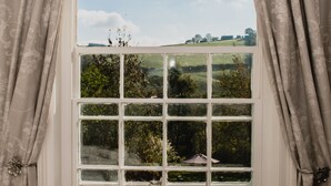 A window with a view of a green landscape, curtains, and a white frame. - Penygelli Country House Apartments (Newtown)