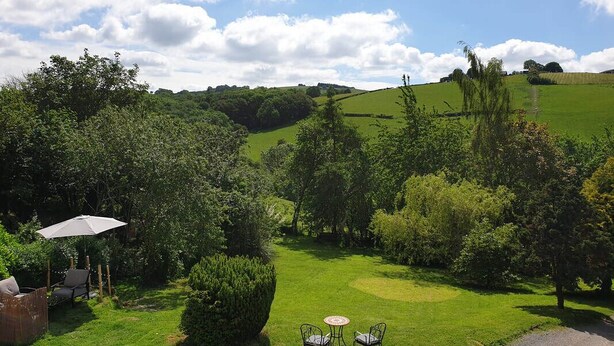 A lush garden with a paved path, a seating area with a table and chairs, and a gazebo with an umbrella. - Penygelli Country House Apartments (Newtown)