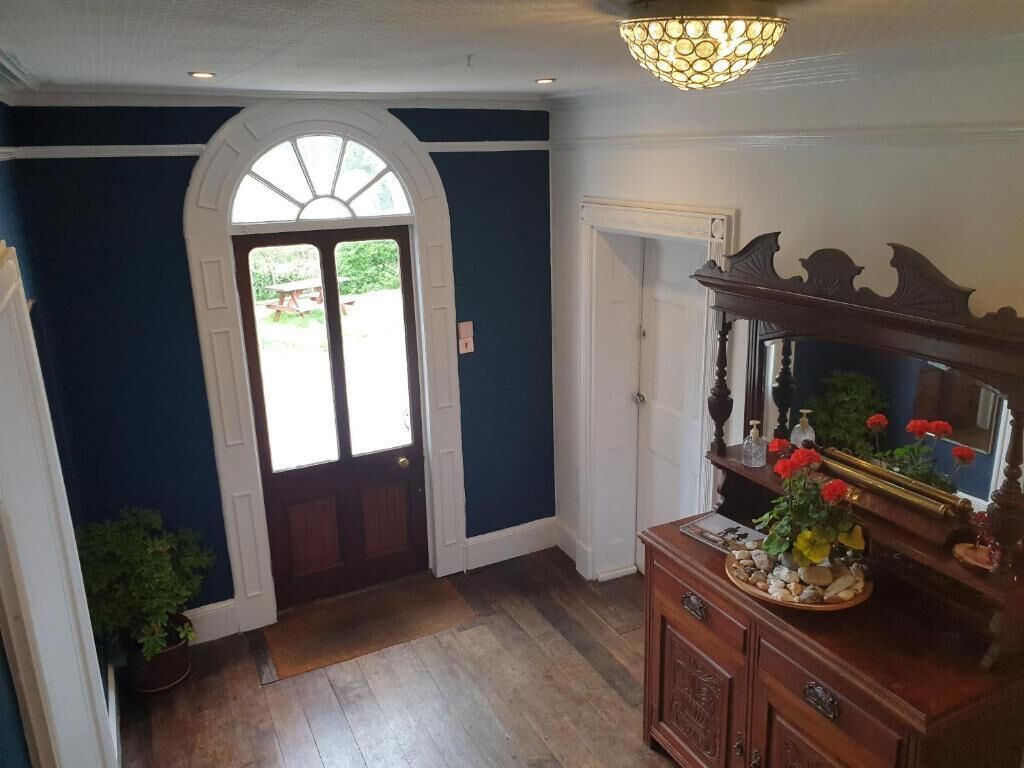 Un couloir avec un plancher en bois, un mur bleu, une porte blanche et un miroir fixé sur un meuble en bois.