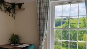 A room with a large window offering a view of green fields and trees. There is a table with chairs and a plant on the wall. - Penygelli Country House Apartments (Newtown)