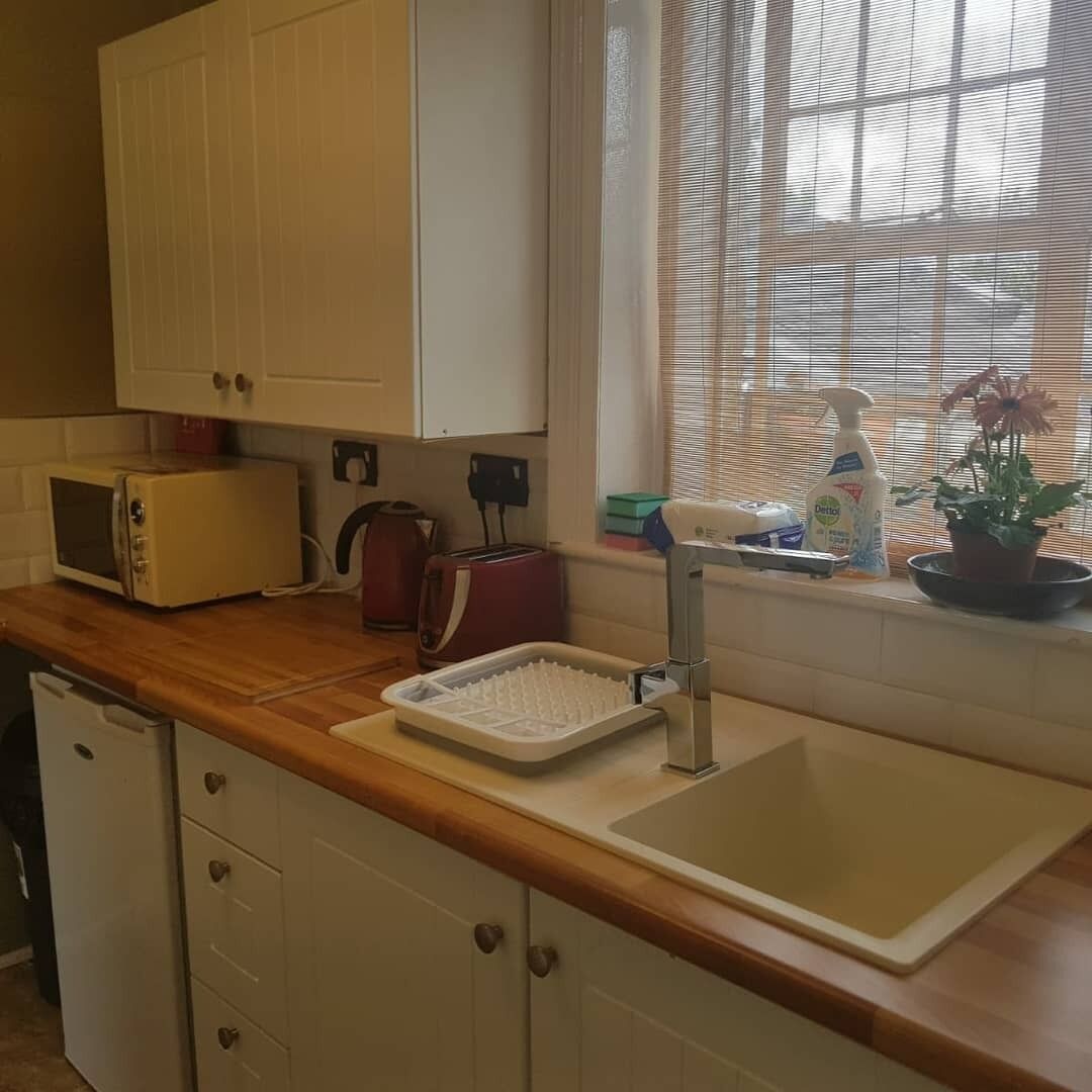 A kitchen with a wooden countertop, a white sink, a microwave, a toaster, and a window with blinds.