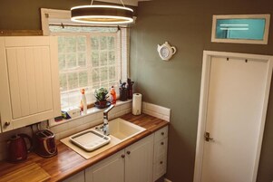 Una cocina con encimera de madera, un lavabo, una tetera y una ventana con persianas.
