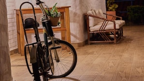 Un vélo est garé à l’intérieur, avec un panier contenant des plantes, une chaise en osier et une table en bois sur laquelle est posé un panneau indiquant « Zone de désinfection ».