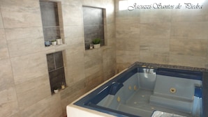 Une salle de spa dotée d’une grande baignoire, de murs carrelés et d’étagères où sont rangés les produits de toilette.