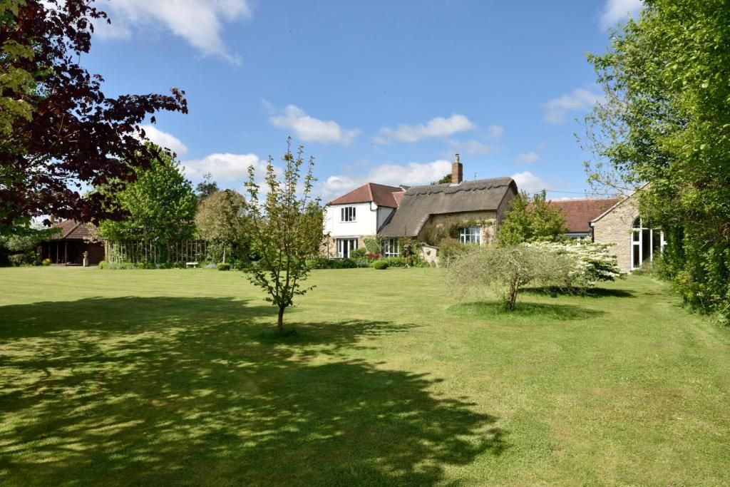 A residential property with a large lawn, a thatched-roof house, and a white building with a red roof.