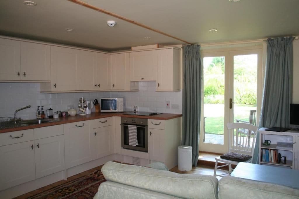 A compact kitchen with white cabinets, a microwave, and a small oven. There is a dining area with a table and chairs, and a large window with curtains.