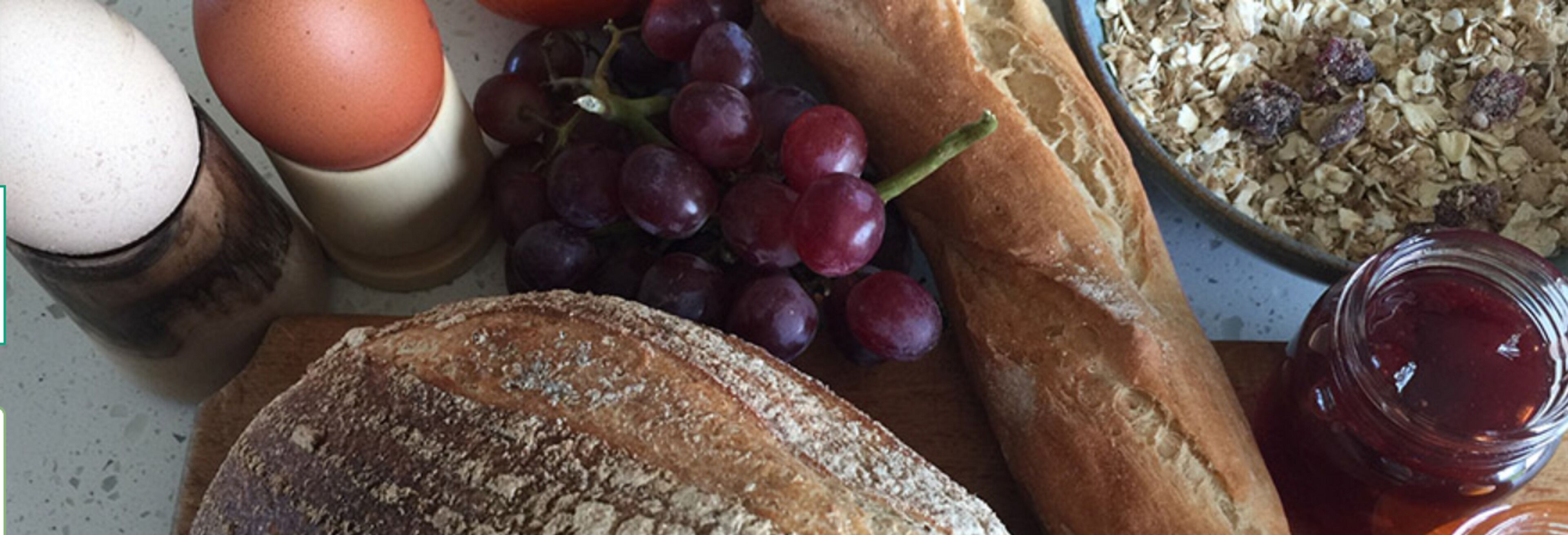 Une table avec du pain, des raisins, un œuf et un bol de céréales.