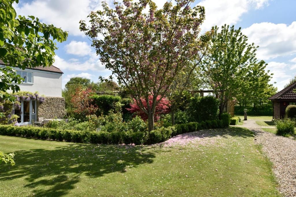 Un jardin bien entretenu, agrémenté de divers arbres et arbustes, d’un mur de pierre et d’un sentier menant à un bâtiment.