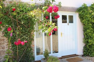 Uma porta branca com um painel de vidro, cercada por vegetação exuberante e plantas trepadeiras.