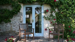 Une terrasse en pierre avec deux chaises en bois et une porte blanche dotée de panneaux de verre.