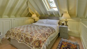 Une chambre avec un plafond en pente, un puits de lumière, un lit recouvert d’une couvre-lit à motifs, deux tables de chevet avec des lampes et un petit tapis.
