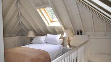A bedroom with a sloped ceiling, a skylight, a bed with white linens, two bedside lamps, and a white railing.