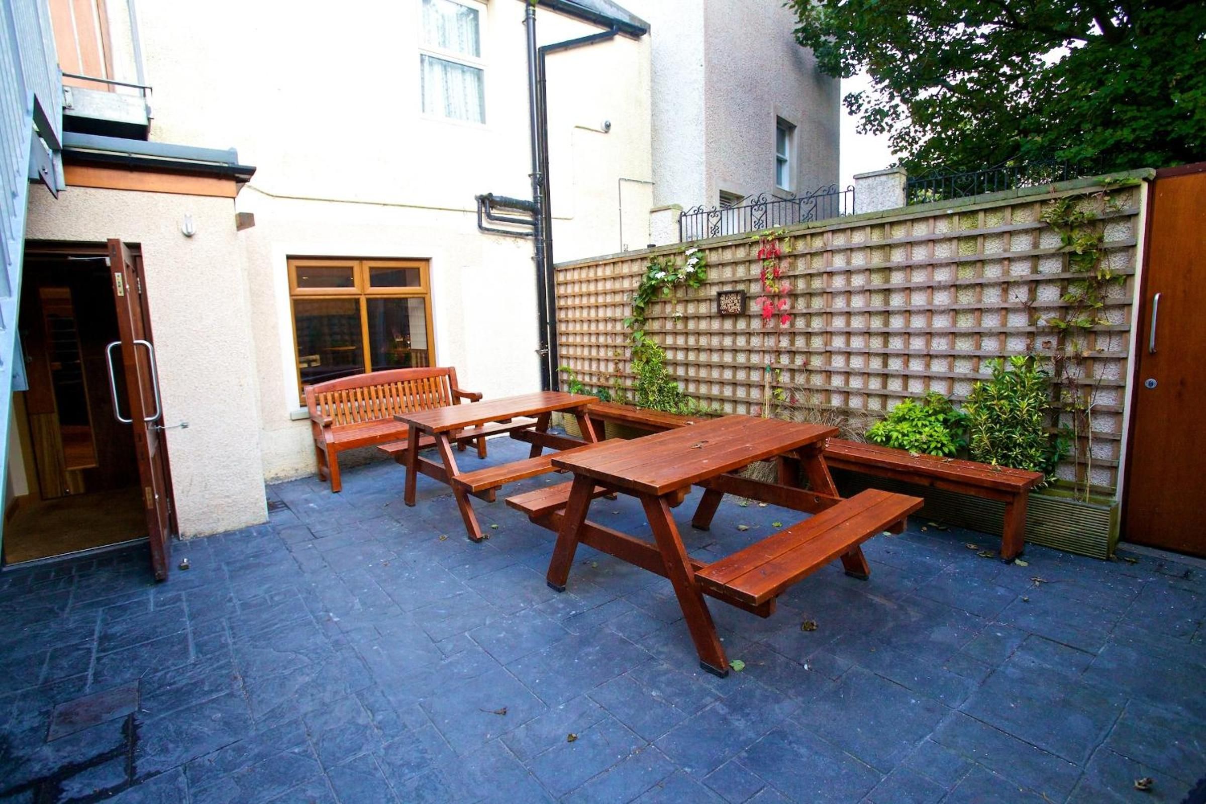 Eine Außenpatio-Terrasse mit Holztischen und -bänken, einem Backsteinboden und einer Wand mit Kletterpflanzen.