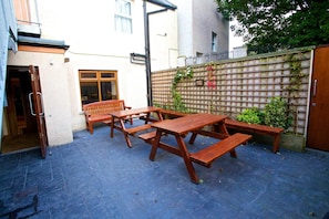An outdoor patio area with wooden tables and benches, a brick floor, and a wall with climbing plants. - St Ola Hotel (Kirkwall)