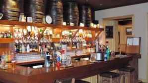 A bar with a long counter, multiple stools, and a variety of bottles and glasses. - St Ola Hotel (Kirkwall)