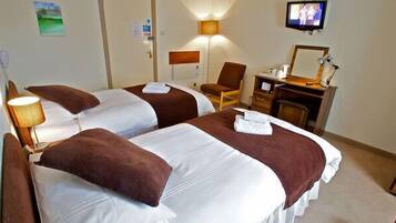 Habitación de hotel con dos camas, un escritorio, una silla, un televisor y una lámpara.