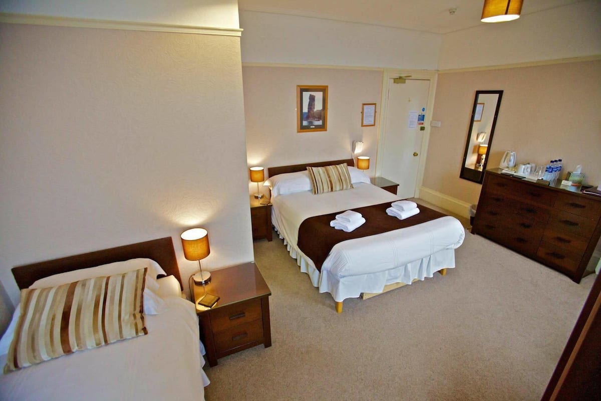 A hotel room with two beds, a dresser, a mirror, and a nightstand with a lamp.