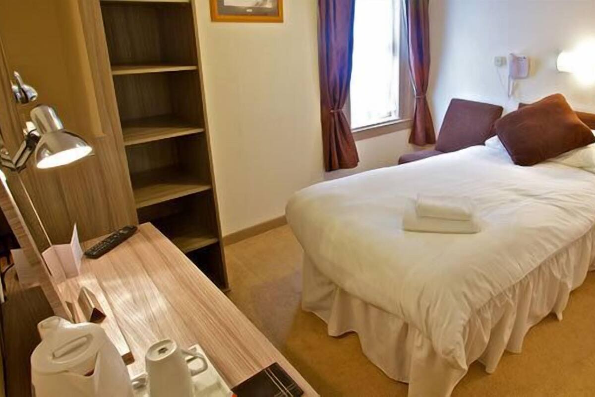 A hotel room with a bed, bedside table, lamp, and a wardrobe.