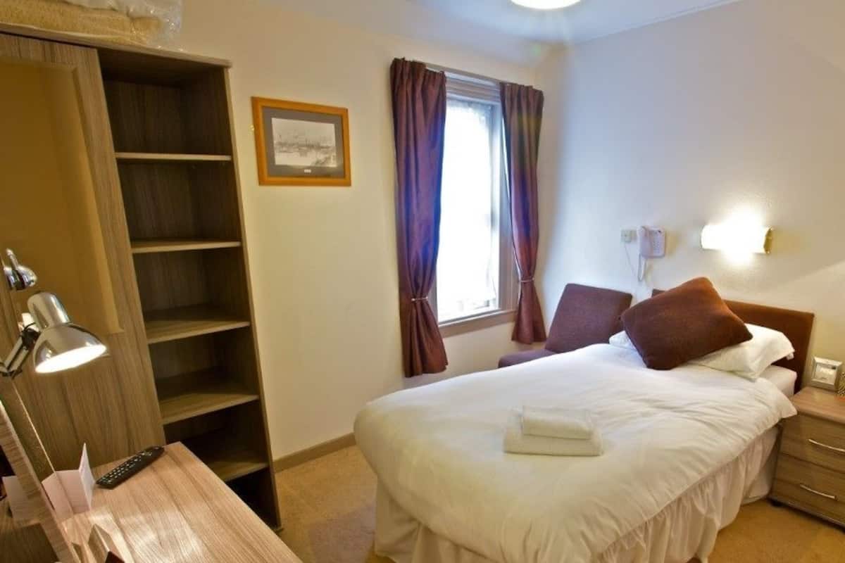 A hotel room with a bed, bedside table, lamp, and a wardrobe.
