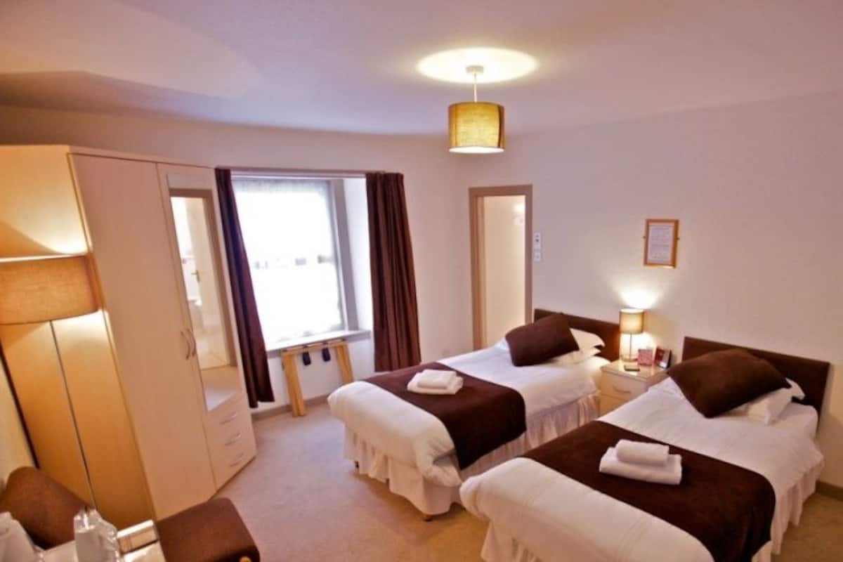 A hotel room with two beds, a wardrobe, a desk, and a window with curtains.