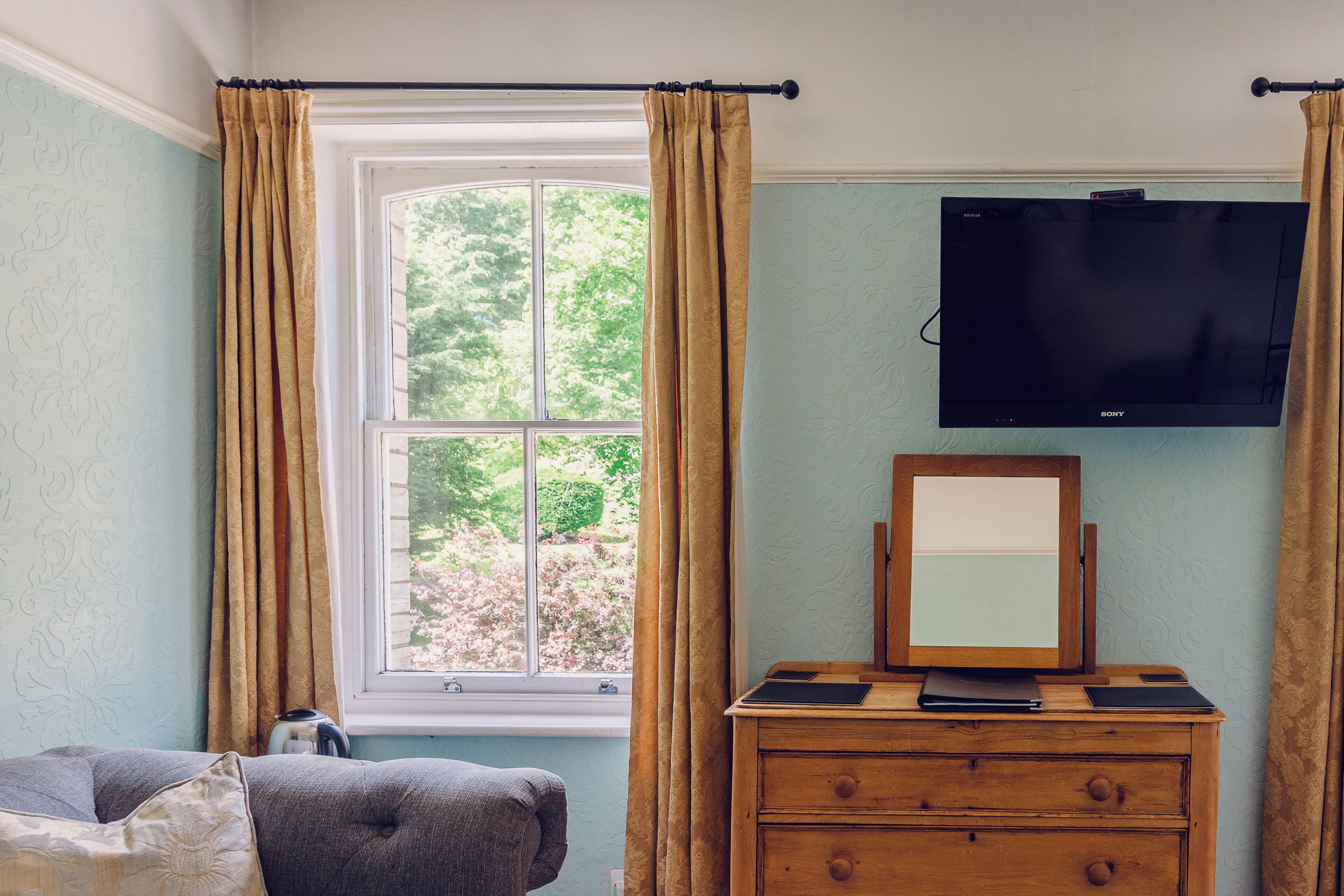 A bedroom with a window, a bed, a dresser, and a mounted television.