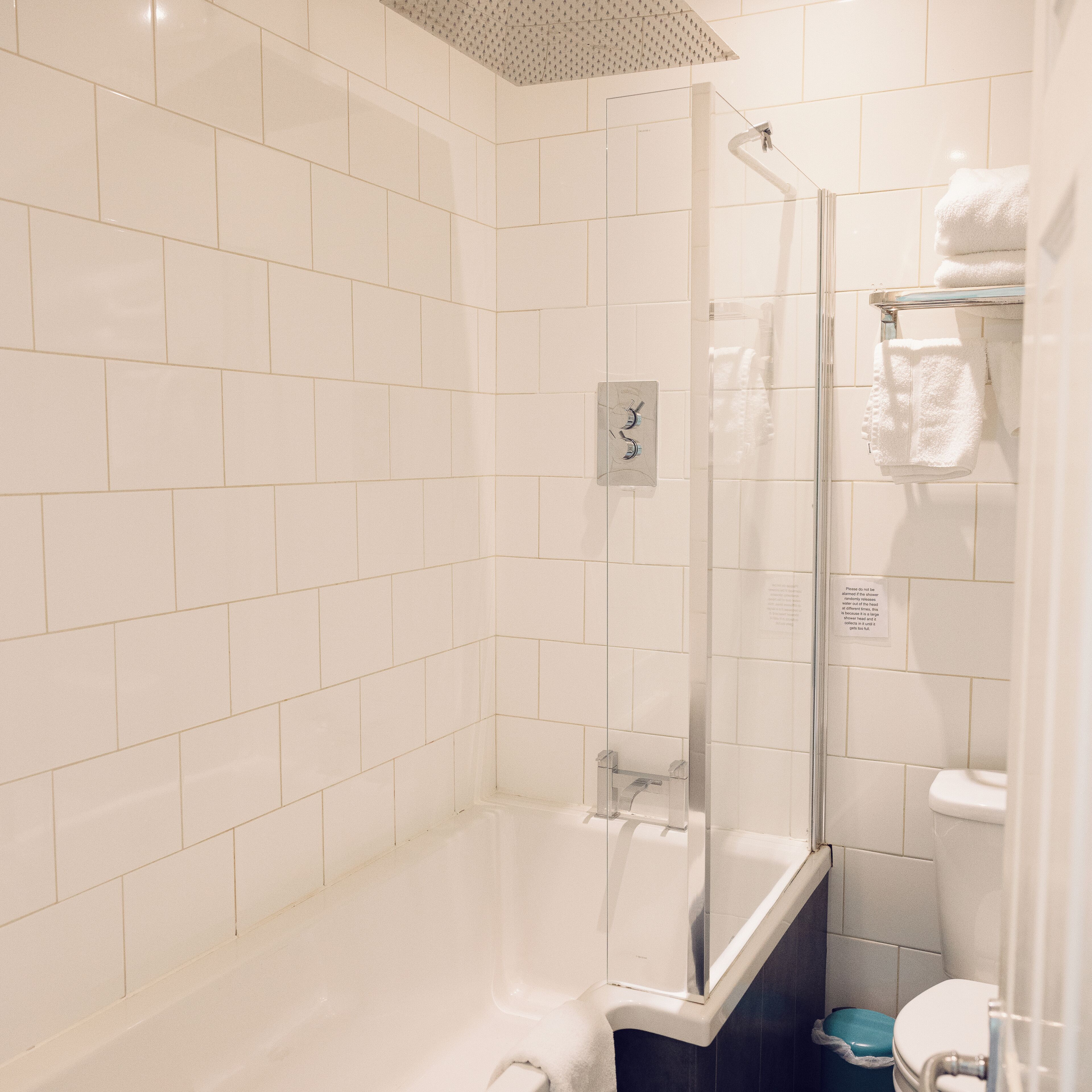 Een badkamer met witte tegels, een glazen douchecabine, een bad en een toilet.