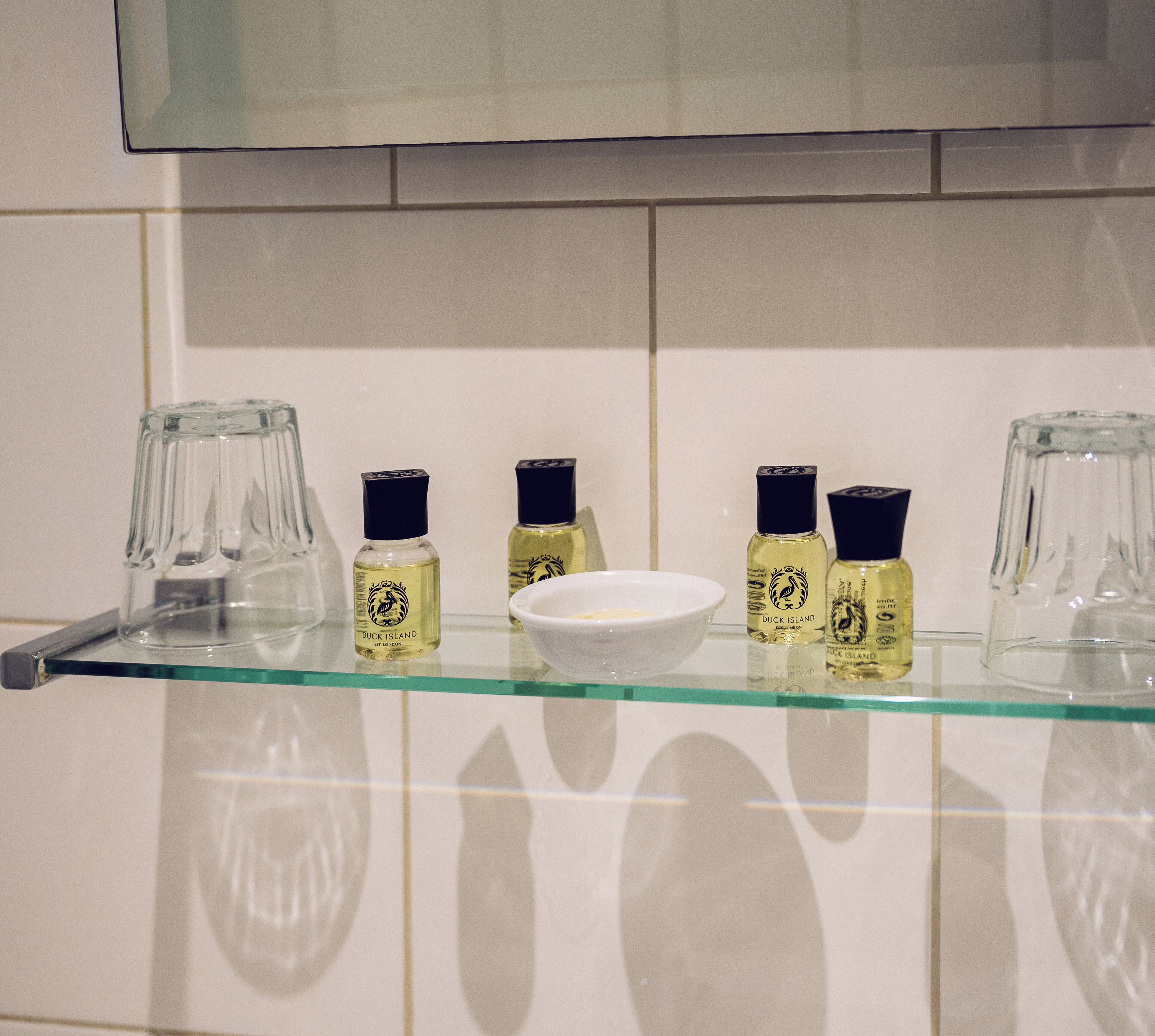 A glass shelf with three bottles of Duck Island gin and a white bowl.