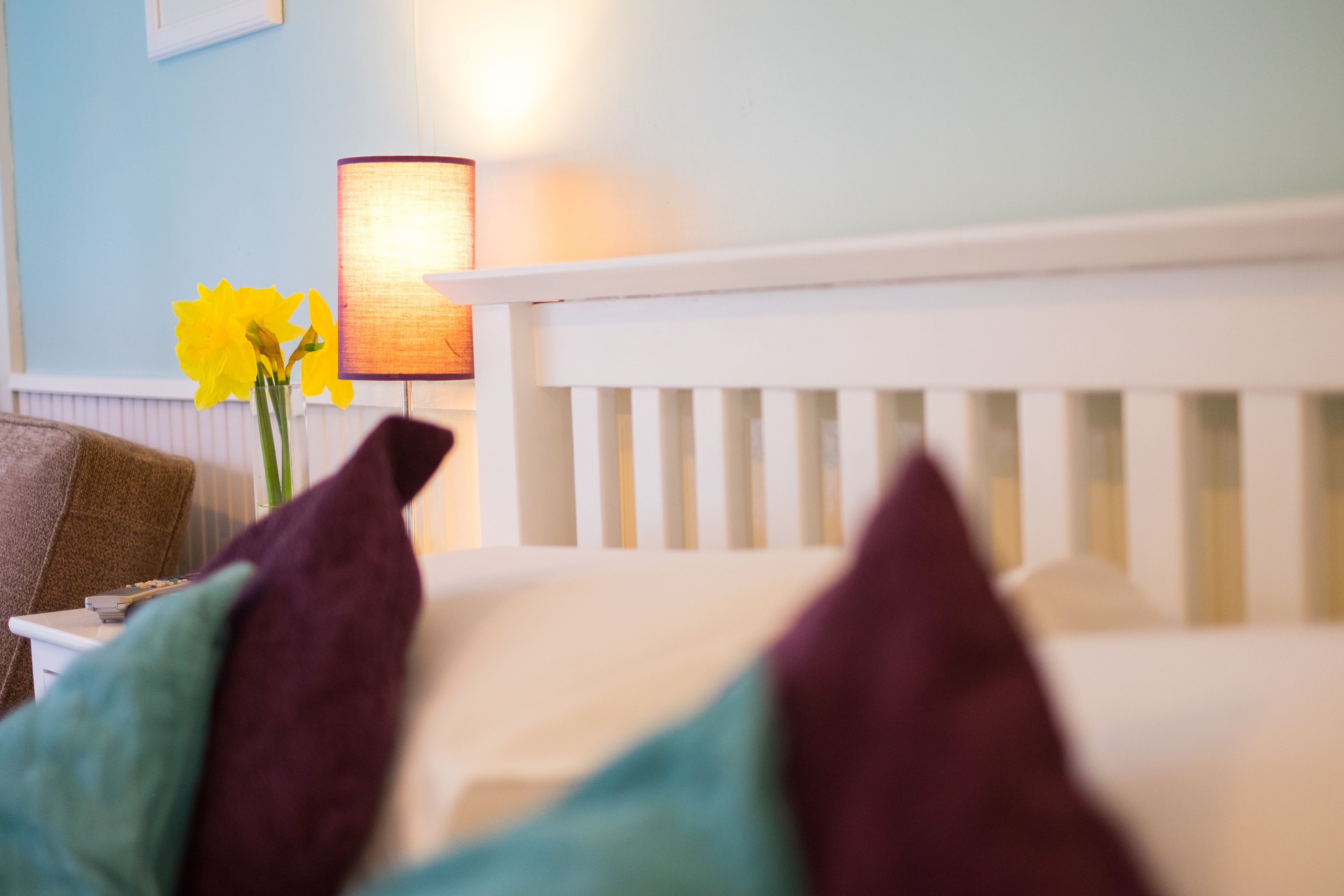 A bed with white headboard, a lamp, and a vase with yellow flowers.