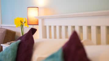 A bed with white headboard, a lamp, and a vase with yellow flowers.