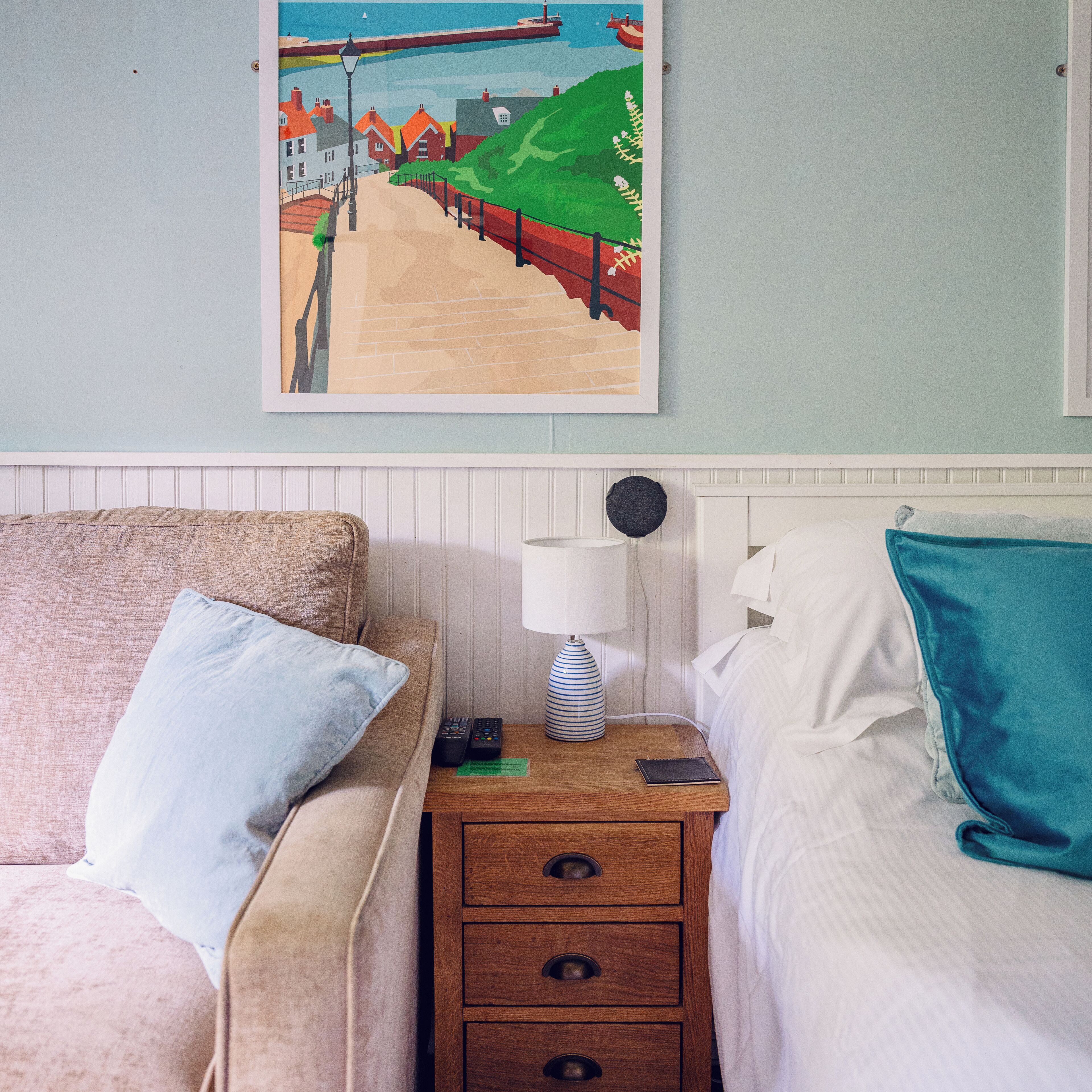 A bedroom with a bed, a nightstand with a lamp, and a framed picture on the wall.